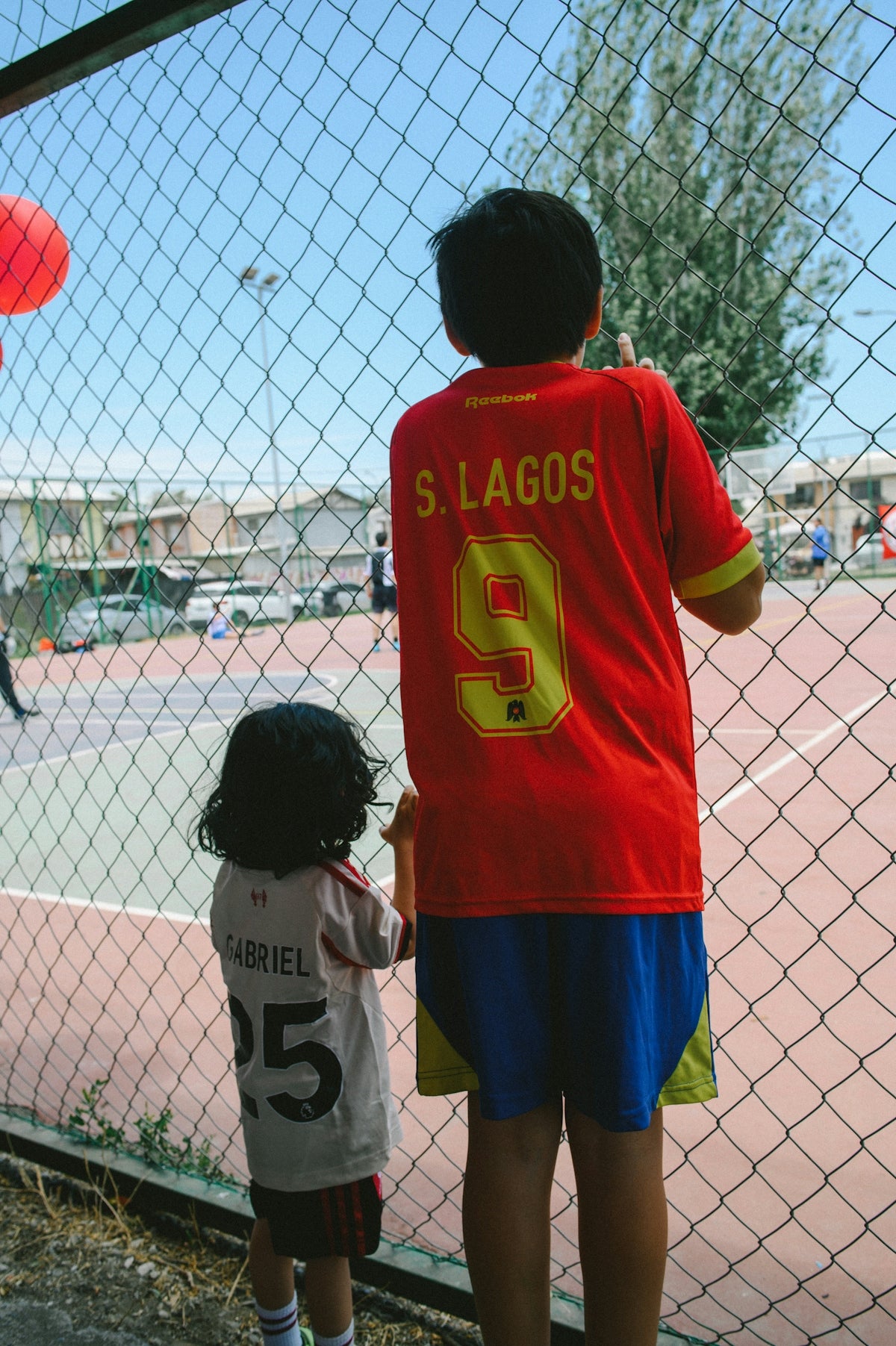 Two children watch a game behind a fence
