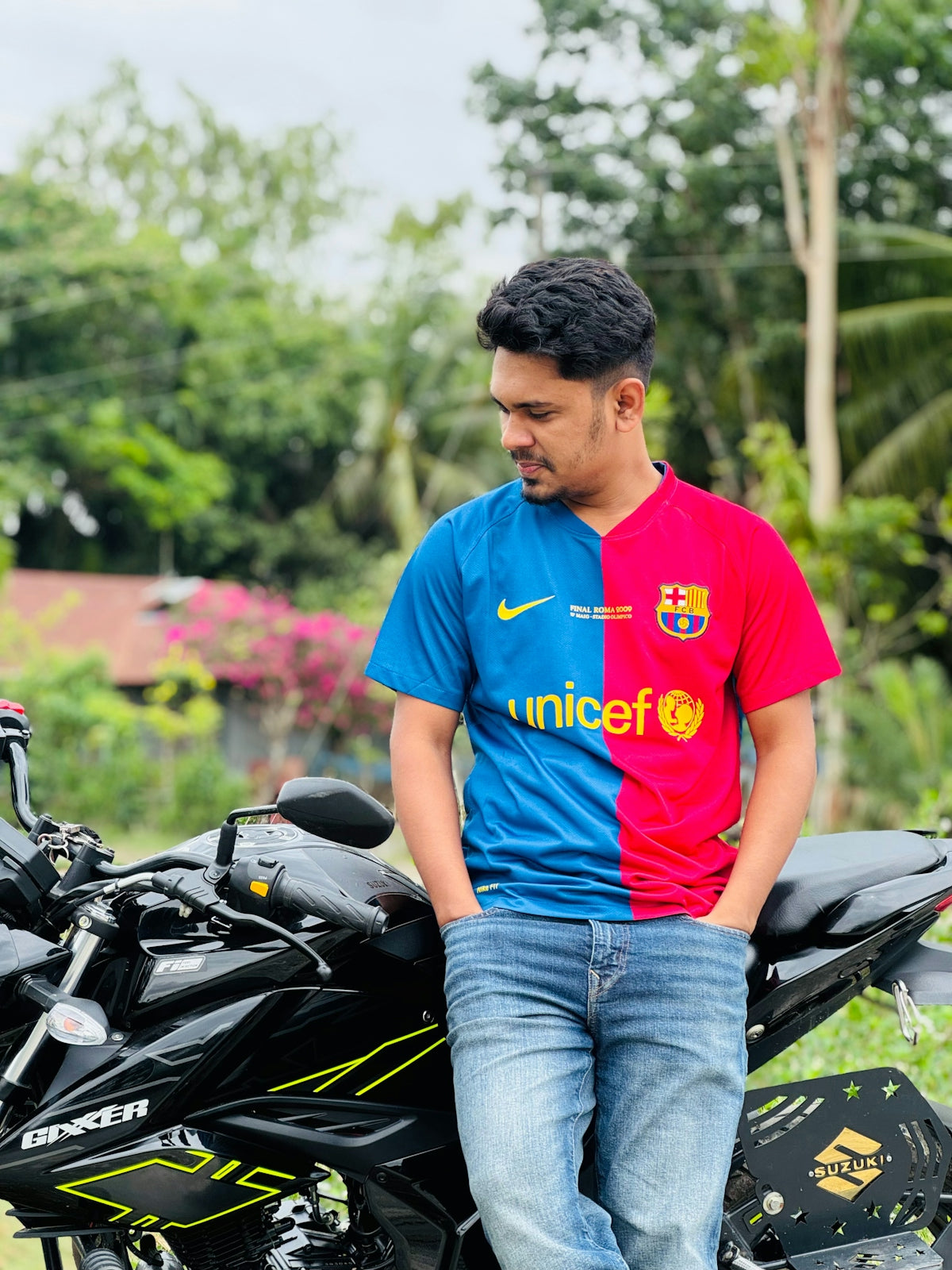 Man in split barcelona jersey leaning on motorcycle.
